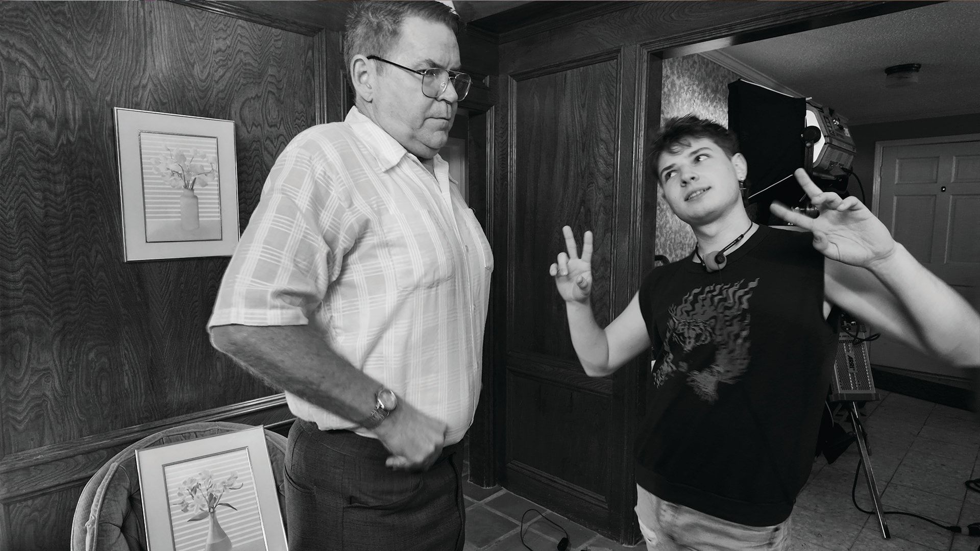 Bill Wise on set next to a young castmate flashing peace signs, in black and white