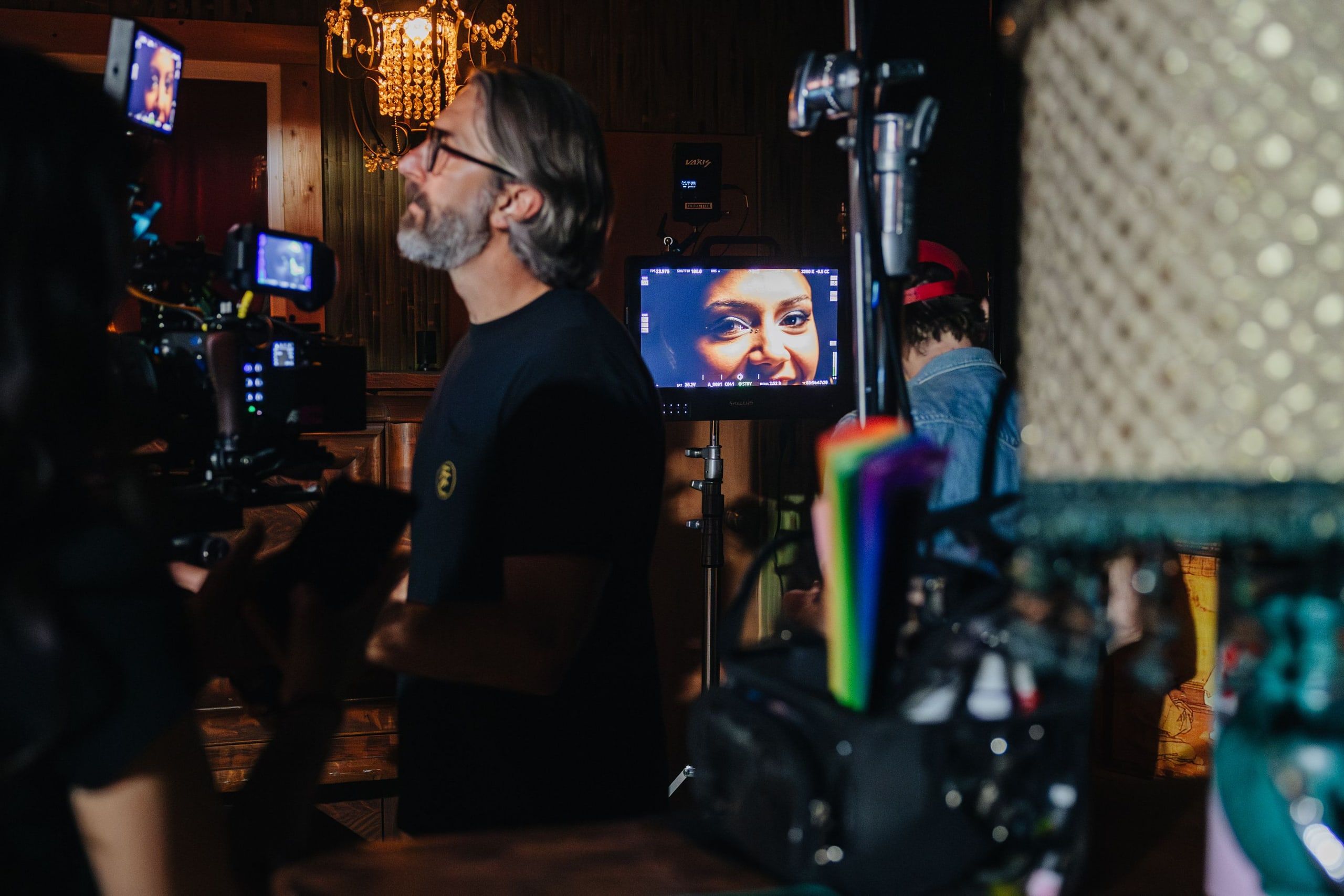A crew member waits on the next take beside the camera, the monitor behind him filled with an extreme close-up of the talent