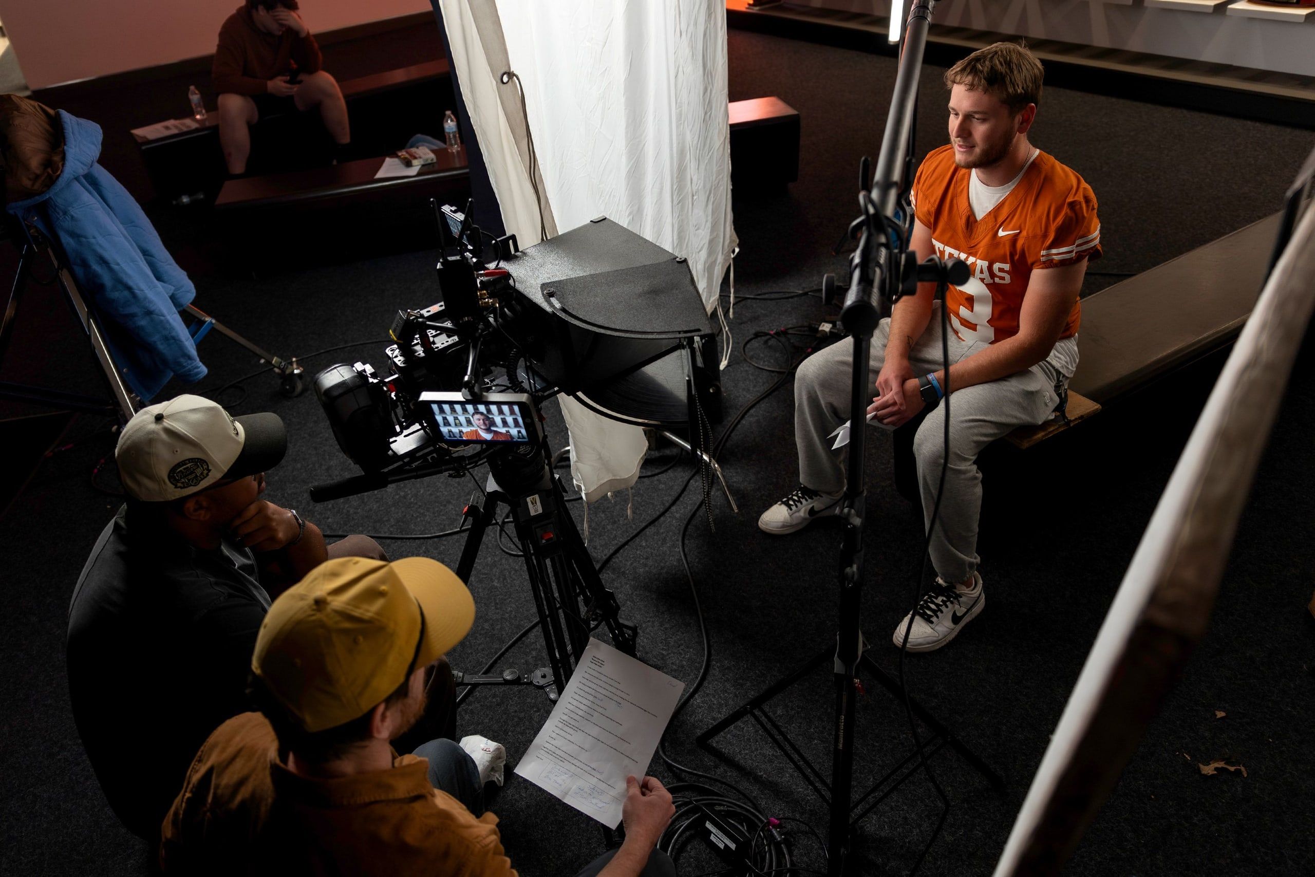 An interview setup in a trophy room: a camera with an eyeline rig, a boom, and a diffusion frame on a football player while the crew follows along