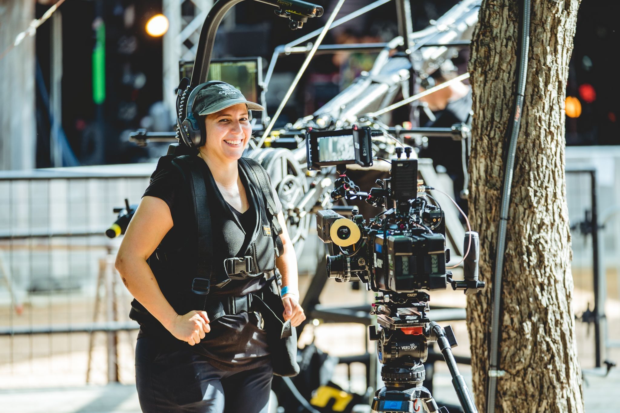 A Steadicam operator in her vest and headset, grinning between takes beside the camera at an outdoor stage