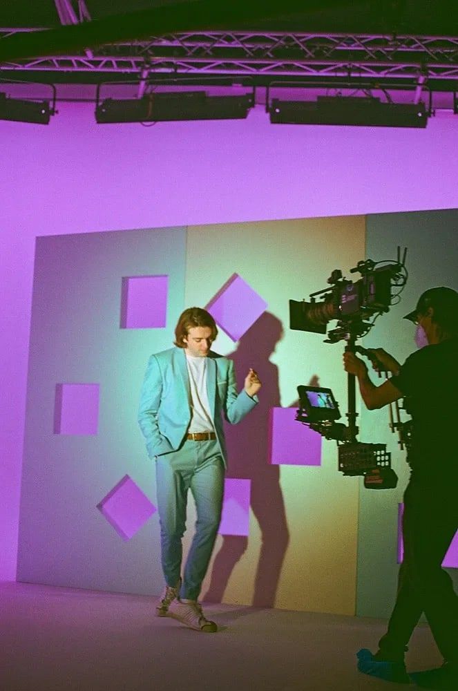 A Steadicam operator tracks a dancer in a teal suit across a lavender set