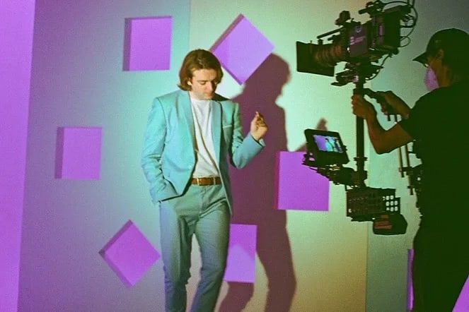 A Steadicam operator tracks a dancer in a teal suit across a lavender set