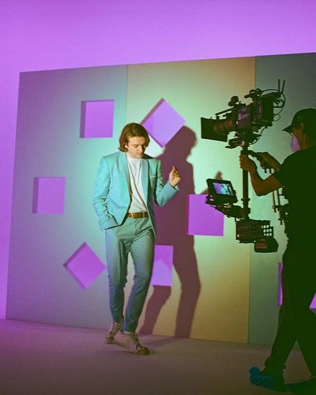 A Steadicam operator tracks a dancer in a teal suit across a lavender set